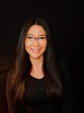 smiling woman with long straight dark hair, wearing glasses and a black shirt