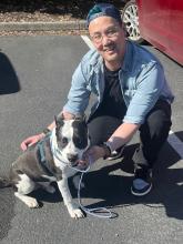 Asian man wearing tshirt with a blue denim shirt over it, baseball cap on backwards squatting with his dog 